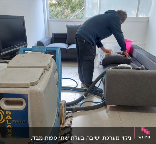 אדם מנקה ספה עם מכונת ניקוי מקצועית